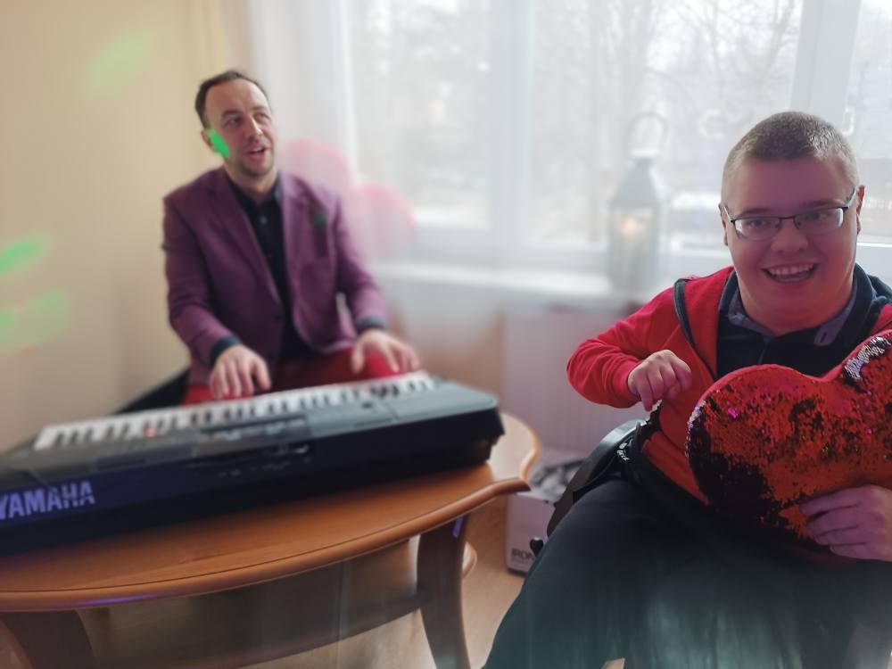 Kierownik Chóru gra na klawiszach, obok siedzi uśmiechnięty podopieczny ŚDS 