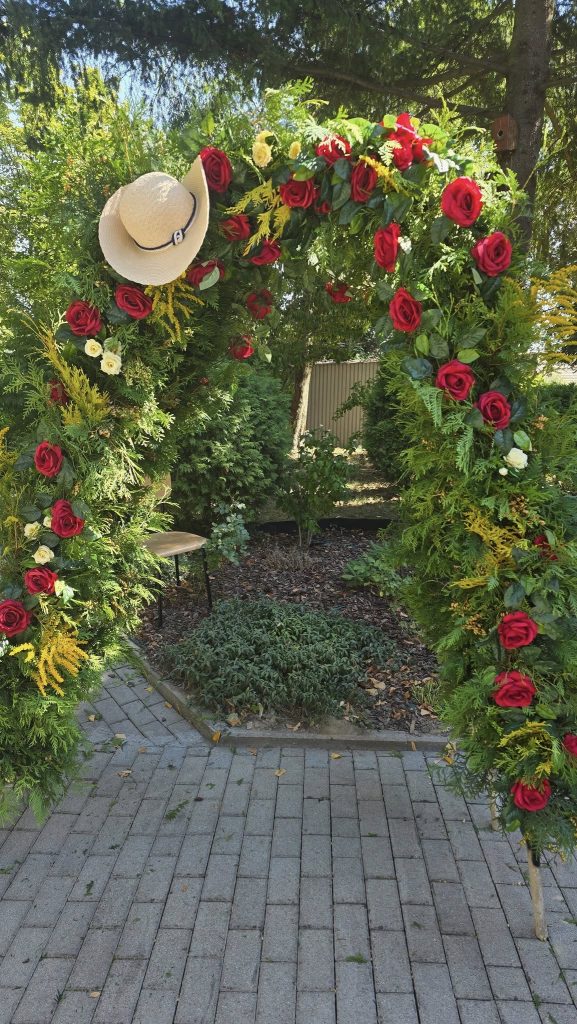 pergola ogrodowa udekorowana gałązkami tui, różami i kapeluszem