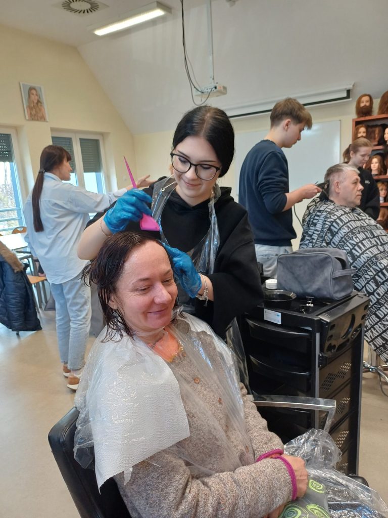 Uczennica klasy fryzjerskiej farbuje włosy Podopiecznej
