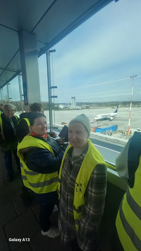 Uczestnicy oglądają płytę lotniska przez okno z terminalu lotniczego