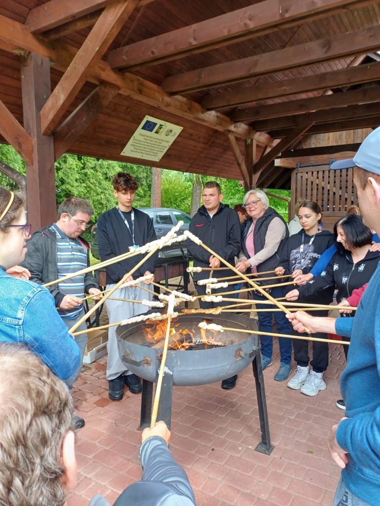 grupa uczestników festiwalu piecze świderki na ognisku
