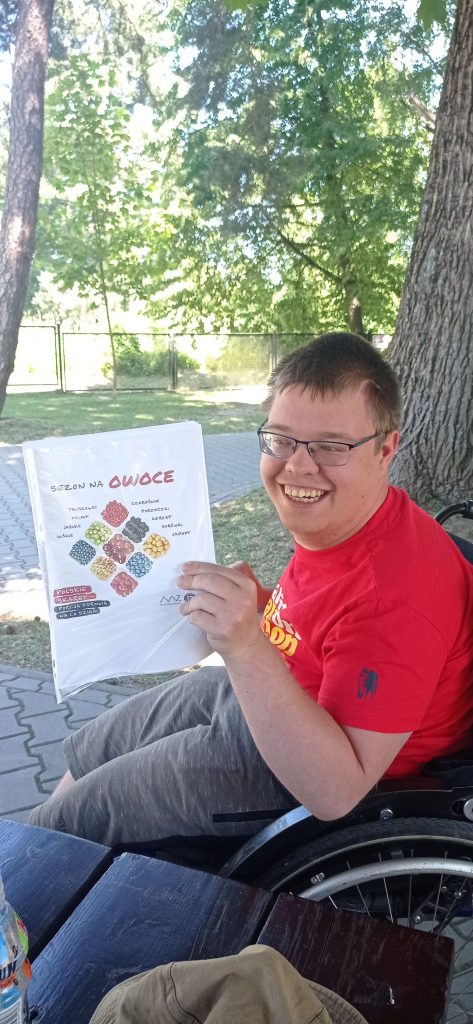 Podopieczny trzyma planszę przedstawiającą owoce sezonowe
