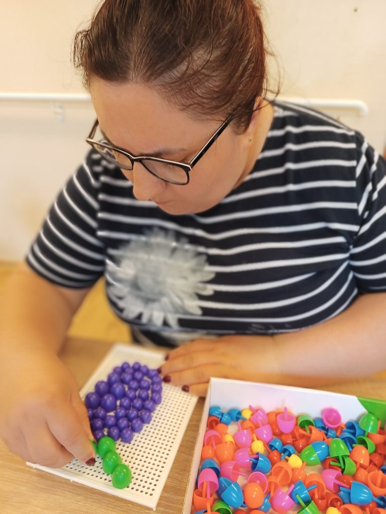 Podopieczna układa owoc na tablicy z wpinkami plastikowymi