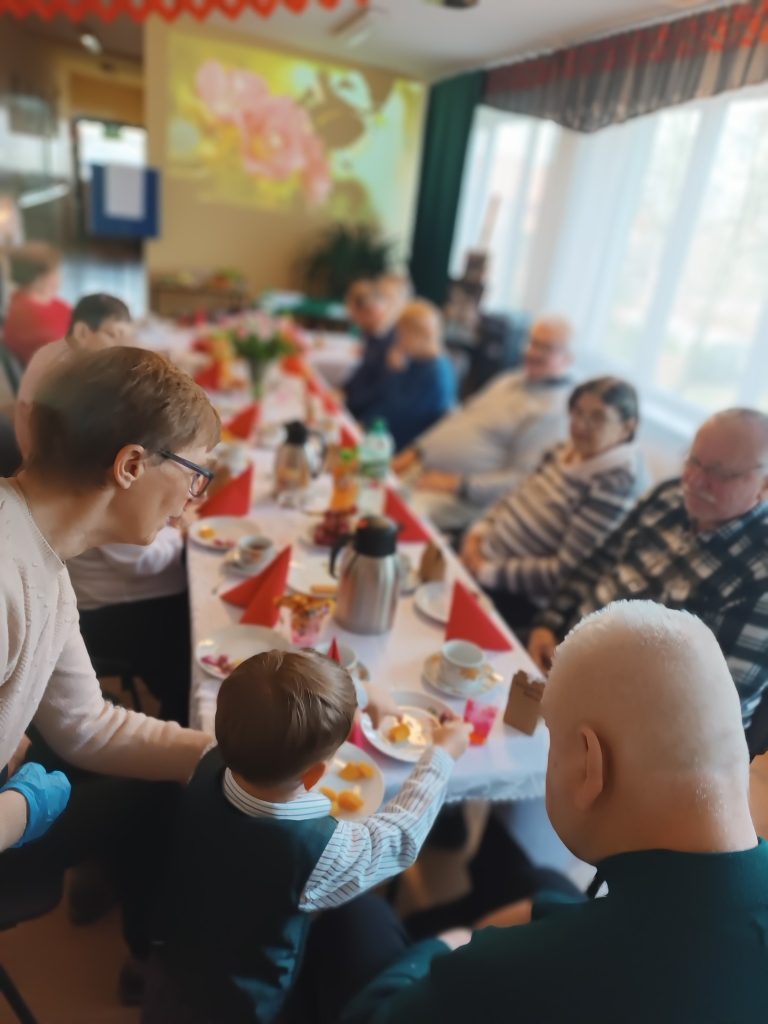 podopieczni siedzą wspólnie przy stole podczas spotkania z okazji Dnia Seniora