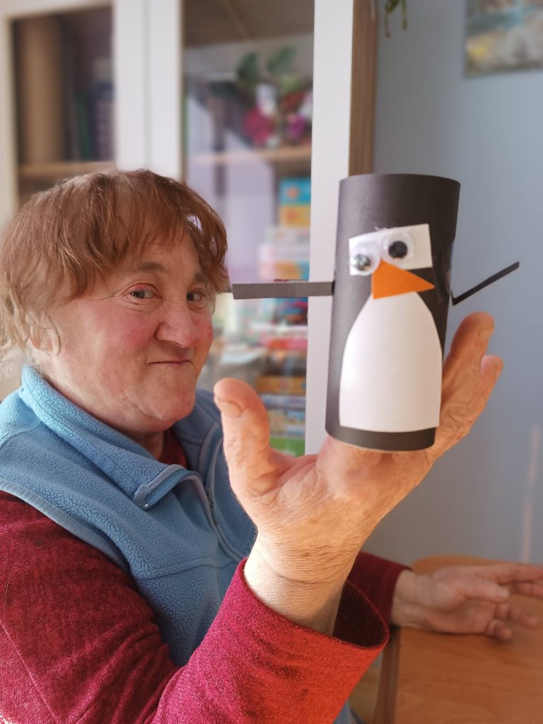 Podopieczna prezentuje pracę plastyczną wykonaną podczas zajęć o pingwinach