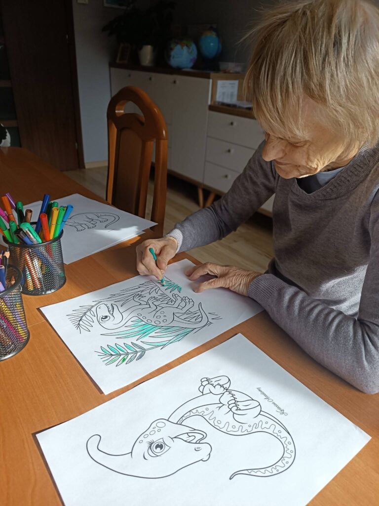 Podopieczna koloruje kredkami obrazek z dinozaurem