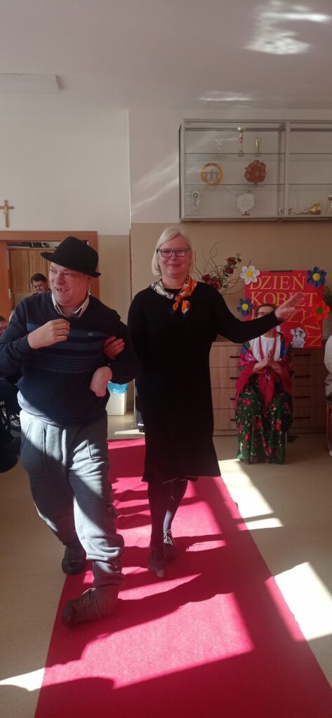 podopieczny z pomocą terapeutki spaceruje po czerwonym dywanie