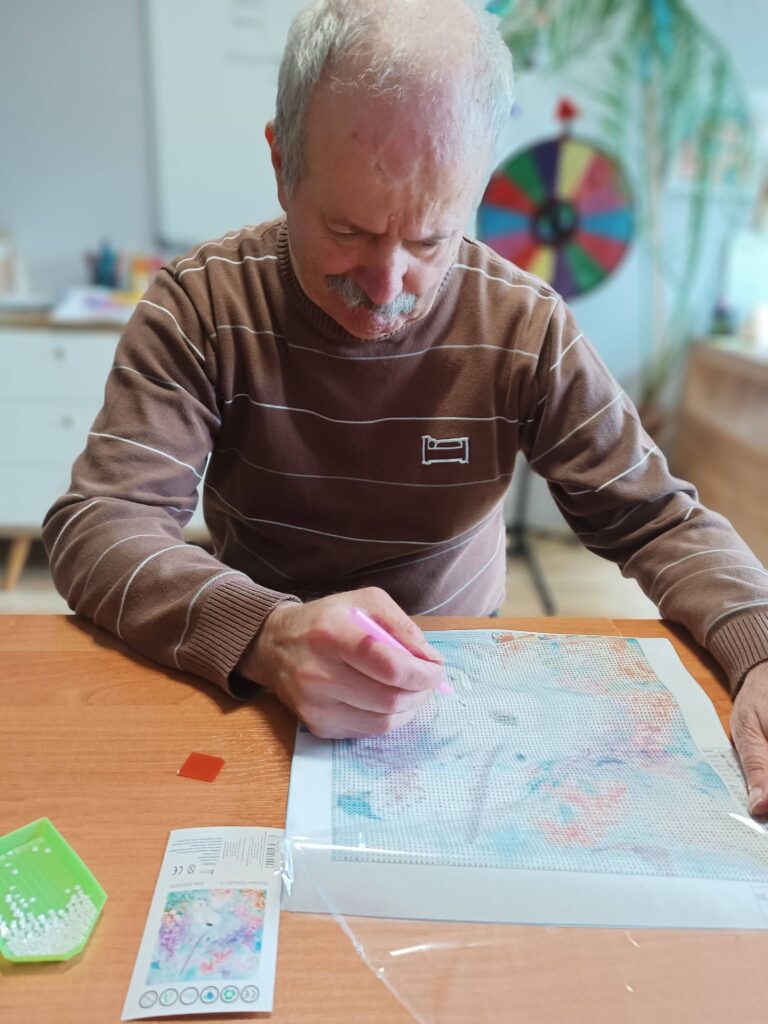 Podopieczny wykleja obrazek metodą haftu diamentowego