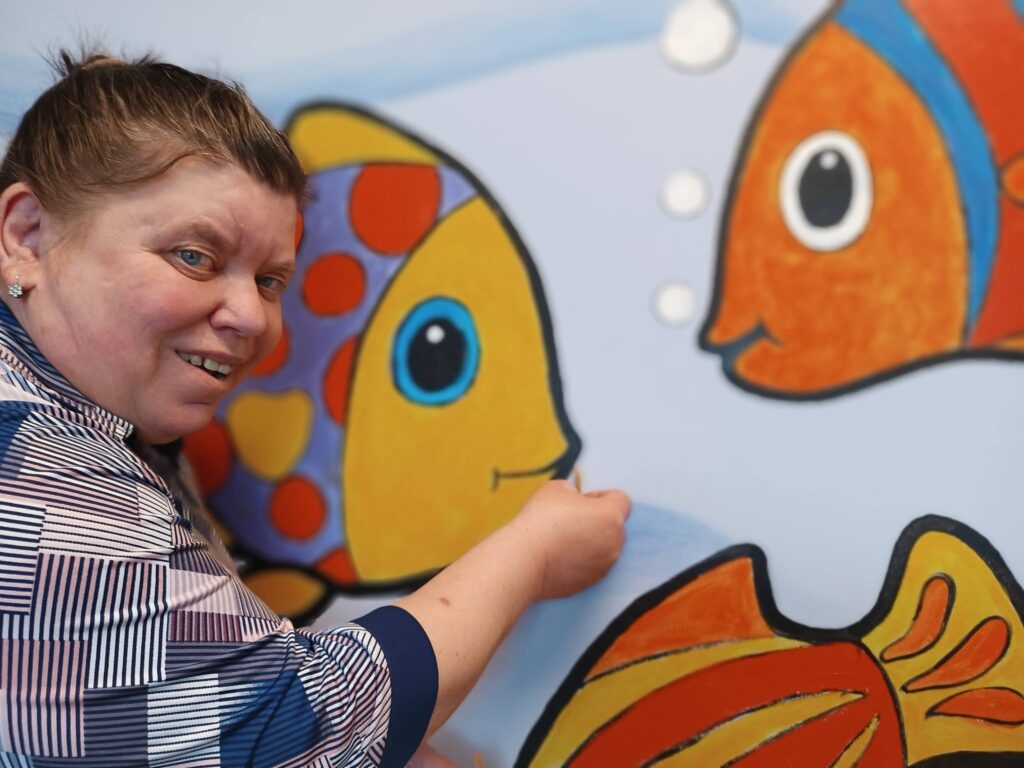 Podopieczna pozuje na tle ściany z namalowanymi kolorowymi rybami