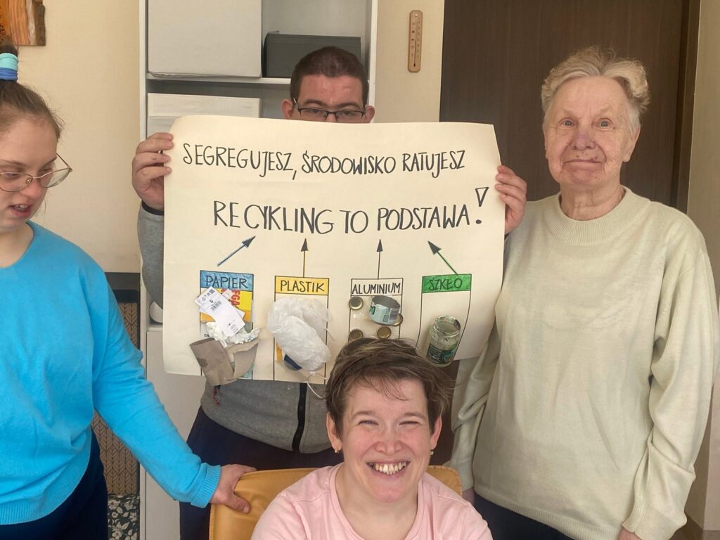 Podopieczni pozują z wykonanym podczas zajęć plakacie o recyklingu