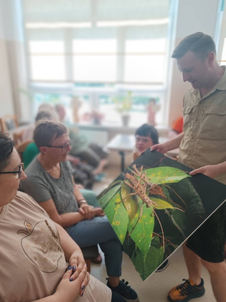 Prowadzący spotkanie pokazuje plakat informacyjny dotyczący patyczaków